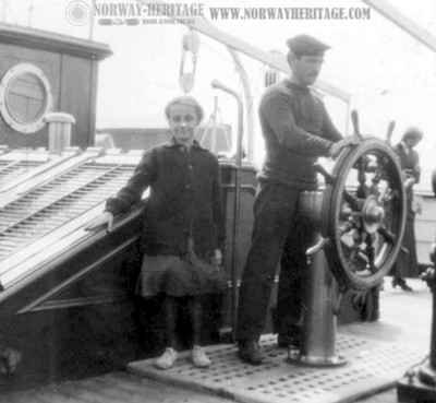 A young girl photographed beside the man at the helm on S/S United States. The picture was taken by a passenger on a voyage in July 1913